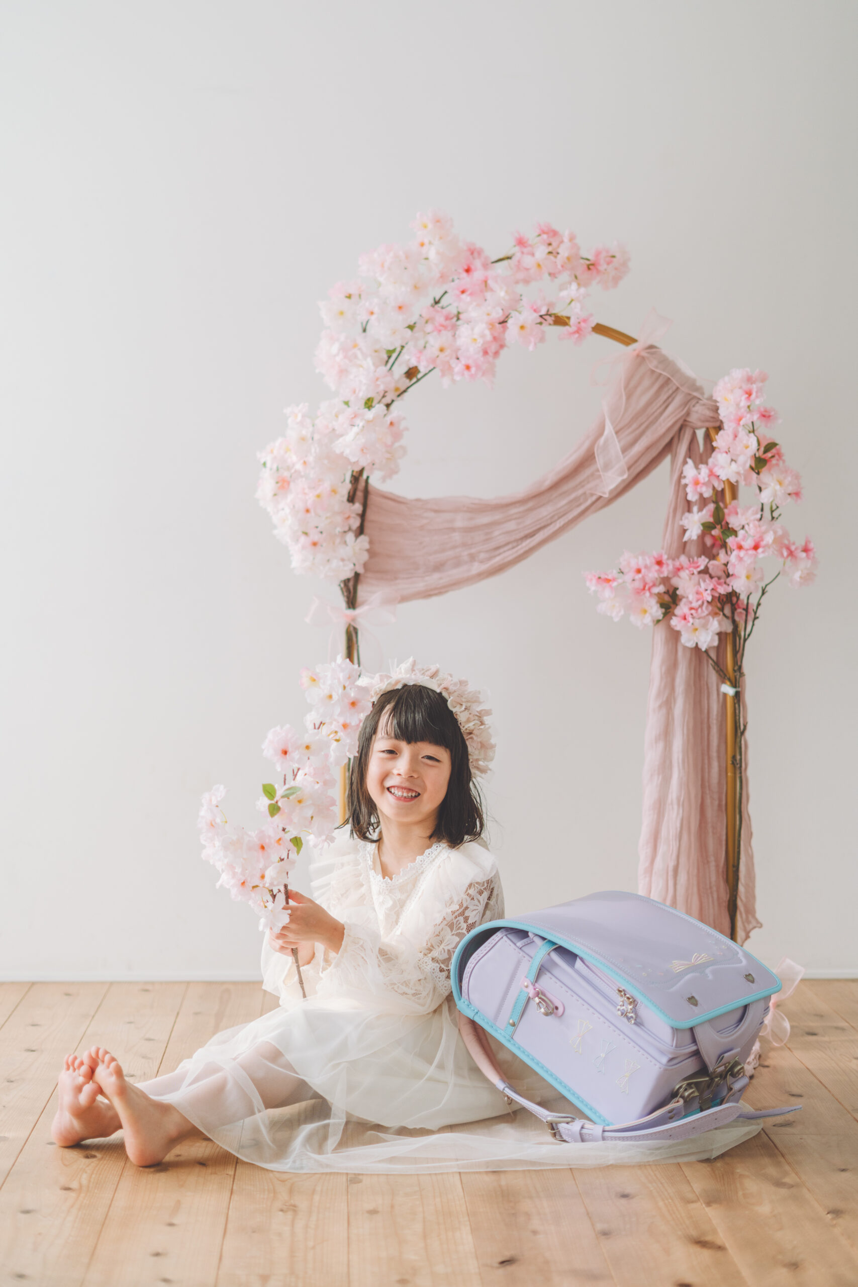 桜に囲まれた撮影ブースでランドセルを横に座る女の子の入学記念写真